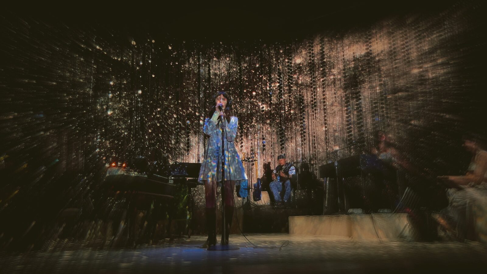 Concert performers on stage behind a textured curtain of light